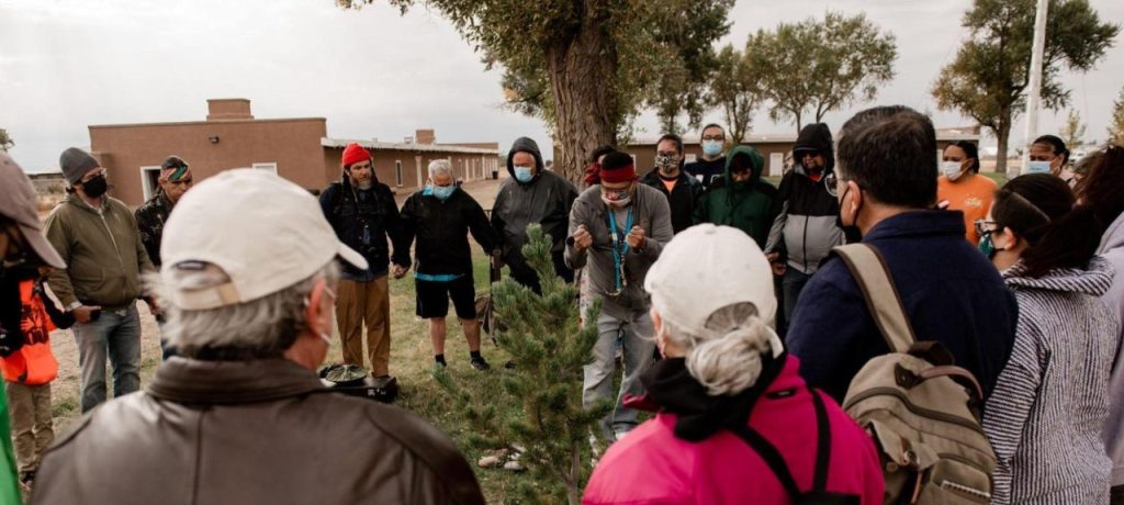 A circle of people watching someone say a blessing over a tree