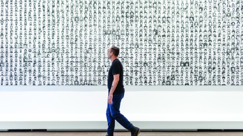 A person walks along a walkway next to a piece of art composed of 0s and 1s.