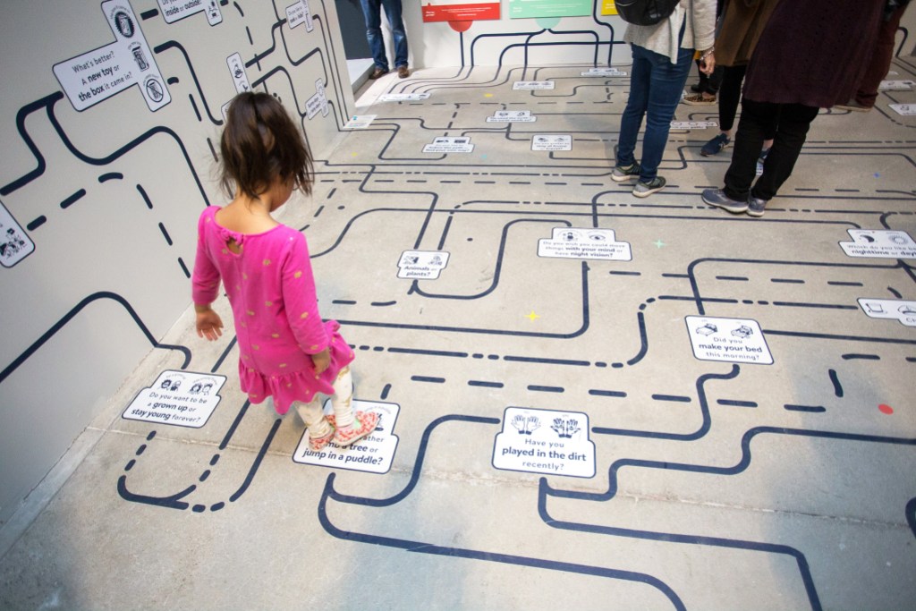 A child stands on top of a map that is painted on the floor and walls.