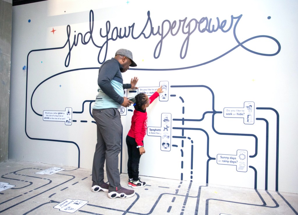 An adult and a child are standing together, studying a map painted on a wall
