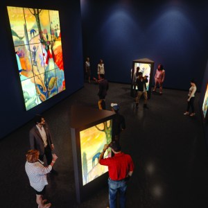 Several people in a darkened gallery with stained glass displays lit from behind. 