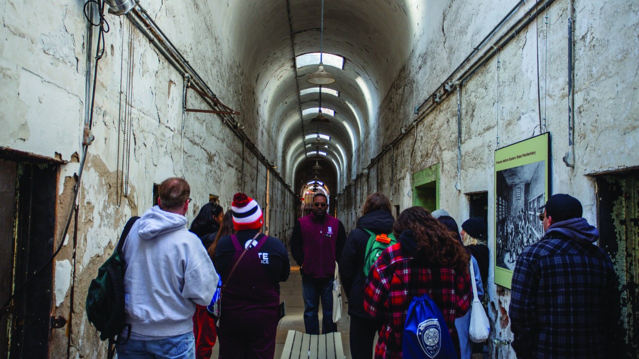 A group of people listen to a tour guide standing in a stark curved ceilinged hallway.