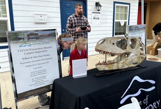 A table set up with a dinosaur fossil and a sign listing supporters of the museum's branch location project.