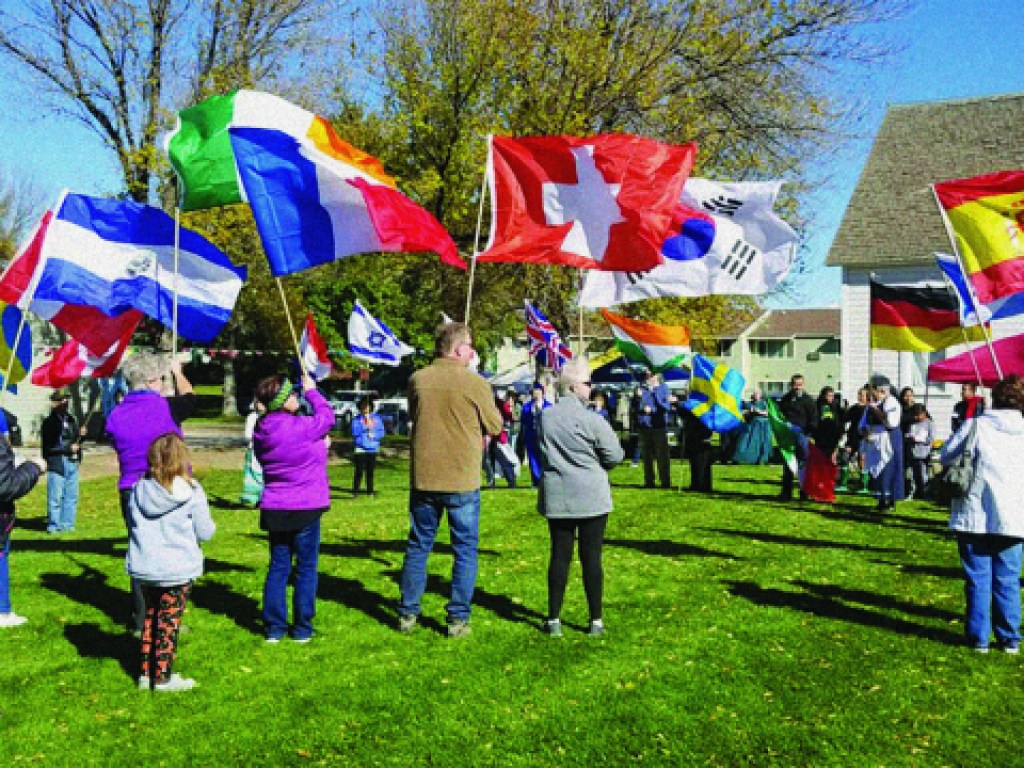 A group of people stand outside in a green grassy area carrying different colorful flags.