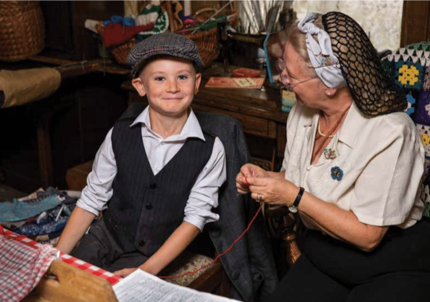 A young person sits next to an older woman who is knitting.