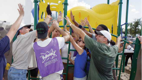 A group of volunteers help erect a piece of playground equipment.