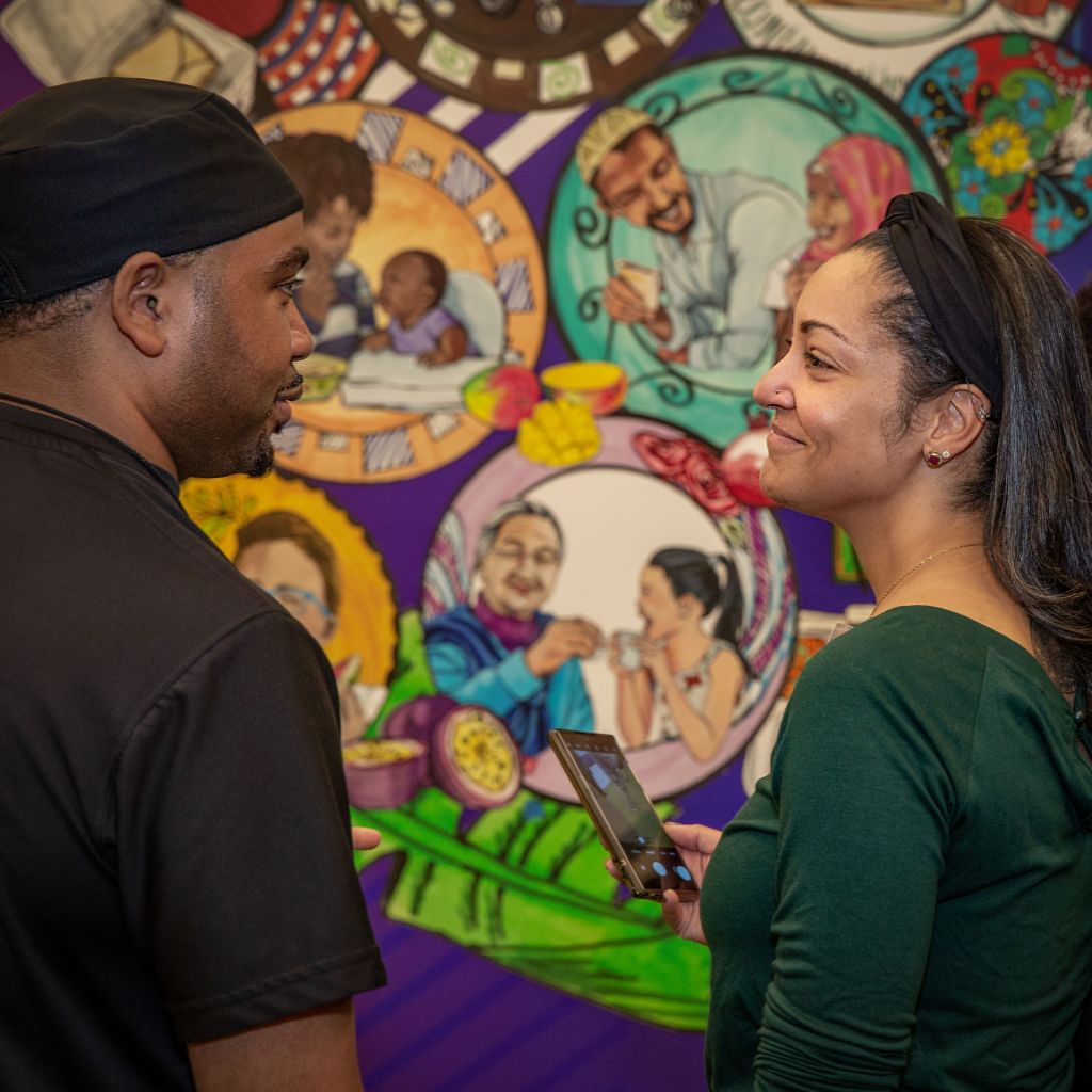 Two people conversing in front of a vibrant mural