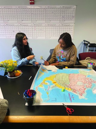 Two young people sit at a table with a map stretched in front of them.