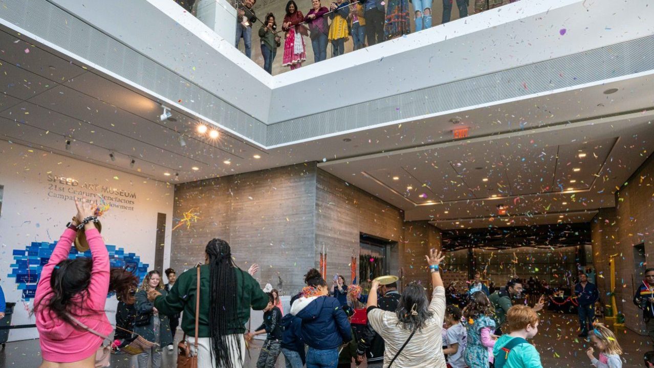 Visitors celebrate Holi with confetti inside a building during Community Day.