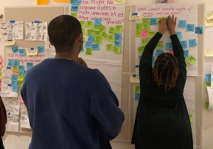 An individual examines a whiteboard filled with colorful sticky notes, with one person adding a note to the collection.