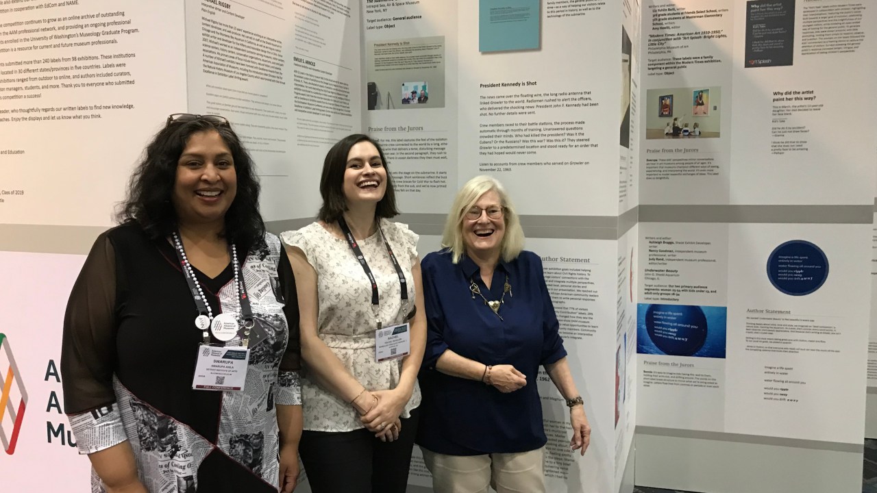 Three people posing in front of posters on display.