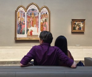 Two individuals on a sofa observing artwork in a gallery.