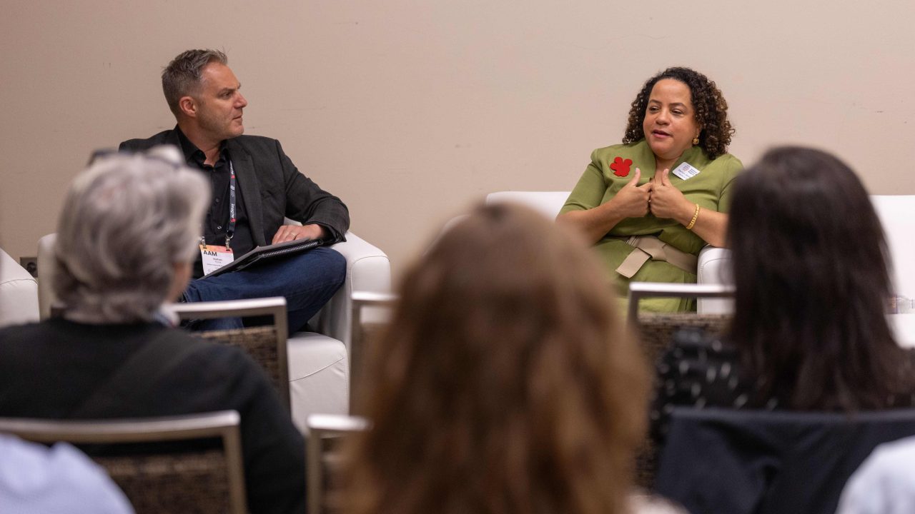 Two people seated on a stage engaged in conversation