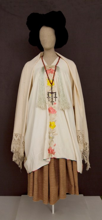 A mannequin wears an long sleeve white top with embroidered buttons and a long brown skirt.