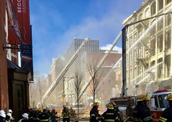 A group of firefighters stand with water hoses shooting water toward a building.