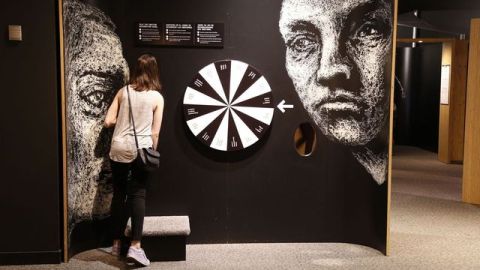 A woman stands looking closely at an exhibit panel with various interactive elements.