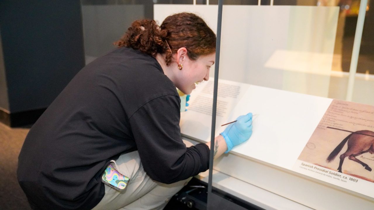 A person working inside of a glass display case while wearing blue gloves