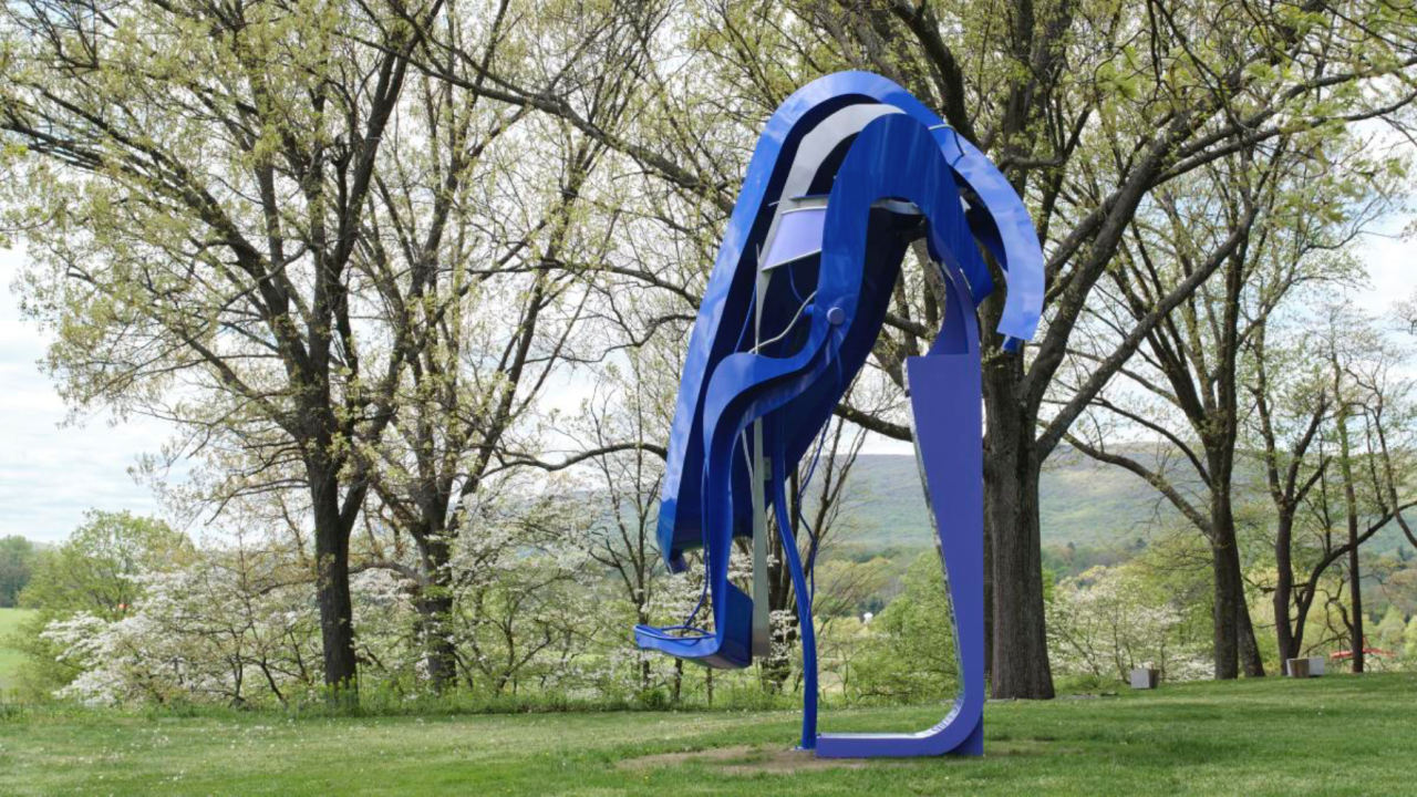 Sculpture made out of blue metal with wavy pieces bent over a central form.