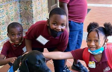 Three young children crouch next to a sitting dog. 