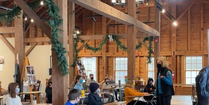 A group of students sit at desks while an instructor teaches before them. 