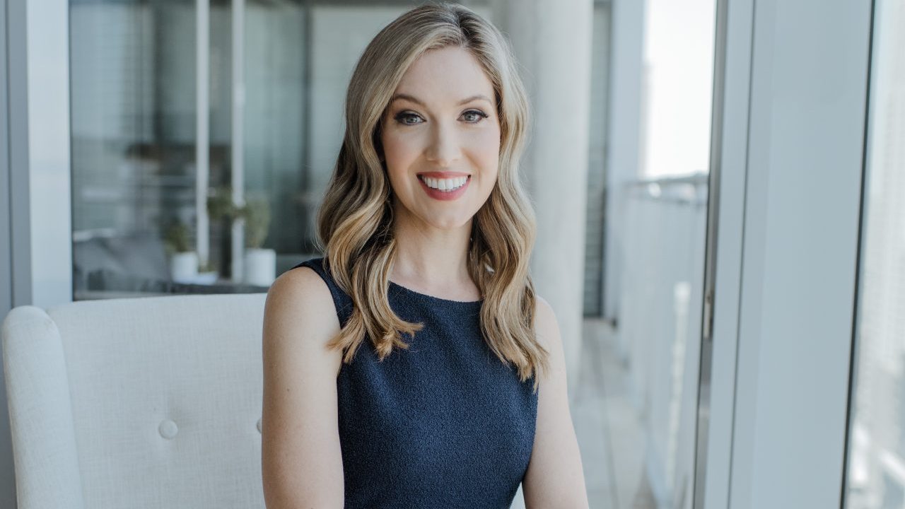 Colleen Dilenschneider sitting in a chair, facing the camera and smiling.