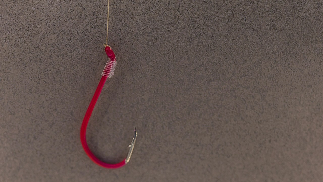 A red fish hook dangles from a clear fishing line in front of a dark gray background.