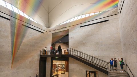 A museum atrium with an installation of thin textiles resembling a rainbow