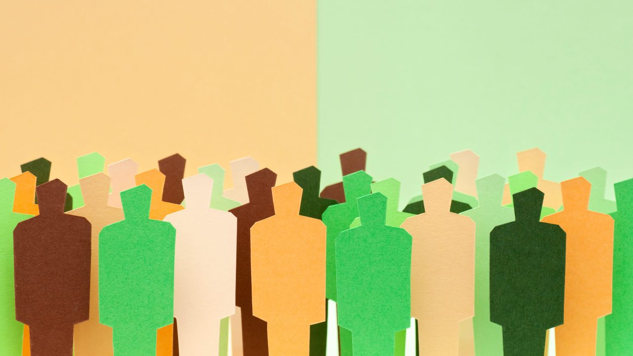 An illustration of paper cut-out human figures in different colors against a background with two divided colors