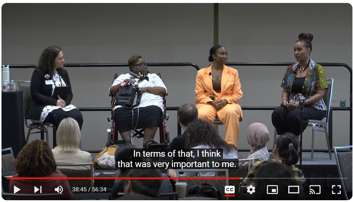 Screenshot of the Imprint Series: Facing Change: Diversity, Equity, Accessibility, and Inclusion video with four panelists on a dais with a crowd of tables and chairs below.