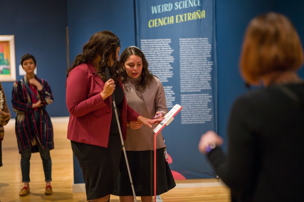 A person holding a cane standing in front of an interactive mount with a guide.