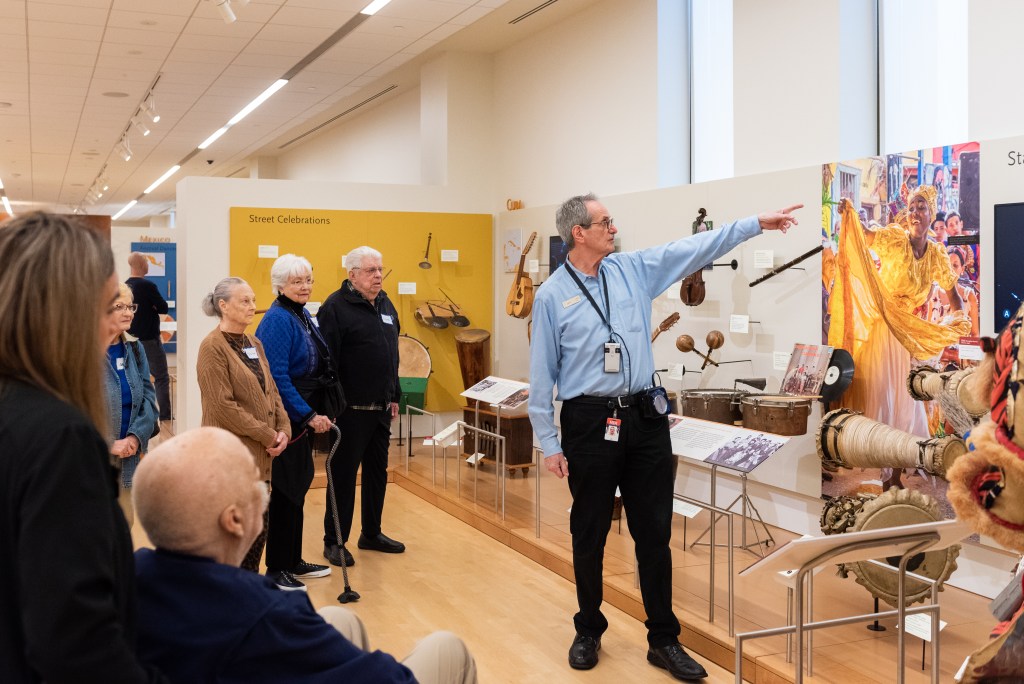 A guide leading a tour of a gallery showcasing musical instruments