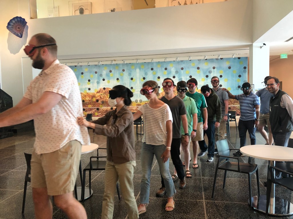 A group of people walking and holding onto each other's backs while wearing goggles