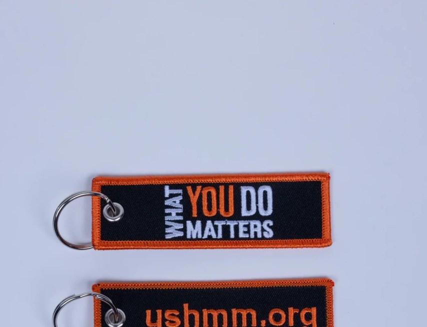 A recto and verso image of a fabric key chain reading "What You Do Matters" on one side and "ushmm.org" on the other side.