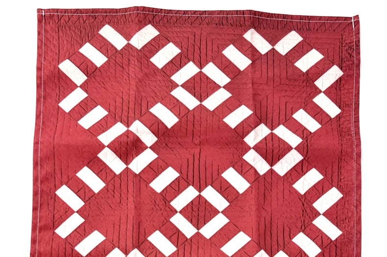 A quilted red tea towel with a white geometric pattern