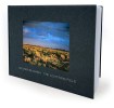 View of a cloth covered book with the leaves showing and an image of a desert scene with a blue sky "framed" in a rectangle on the front cover. 