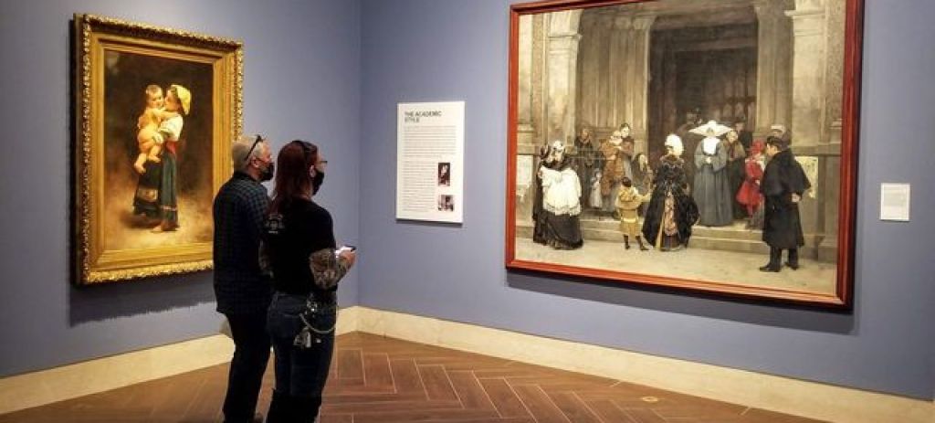 Two visitors stand in a gallery viewing paintings hung on the wall.