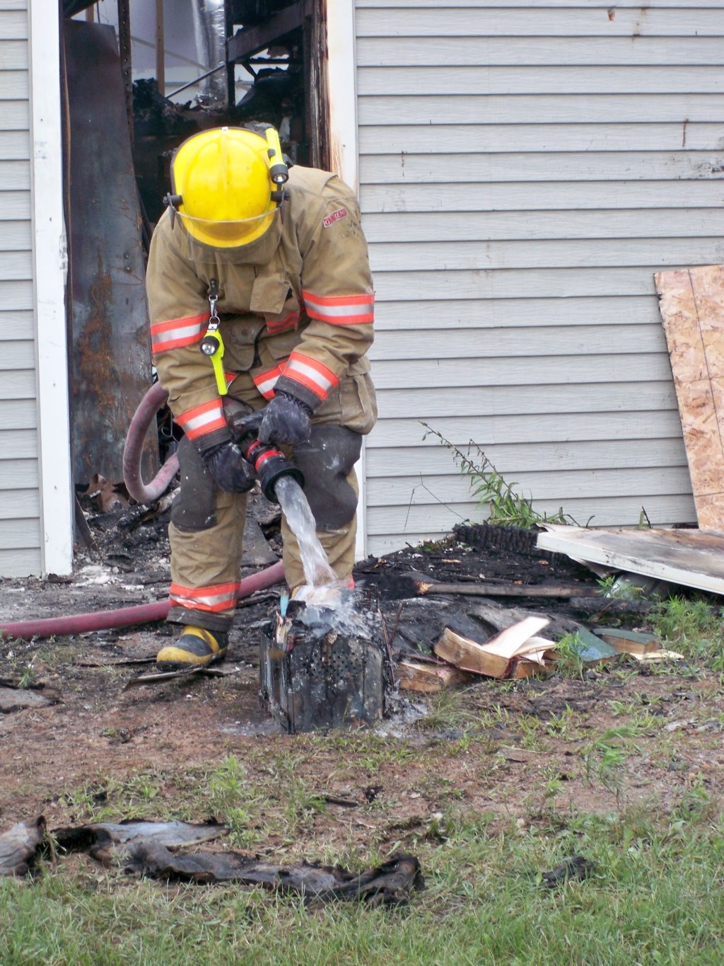 A firefighter is seen outdoors standing over a damaged artifact with a running hose.