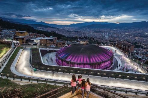 Overhead shot of a group standing at a railing overlooking the top of a large round domed structure at night with purple lights reflecting on the roof.