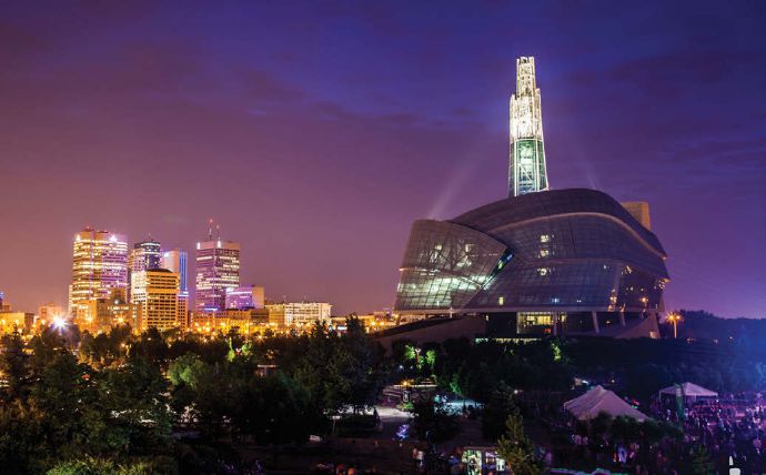 Night skyline with a towering highrise with lights shining on it and the museum in the foreground also with lights.