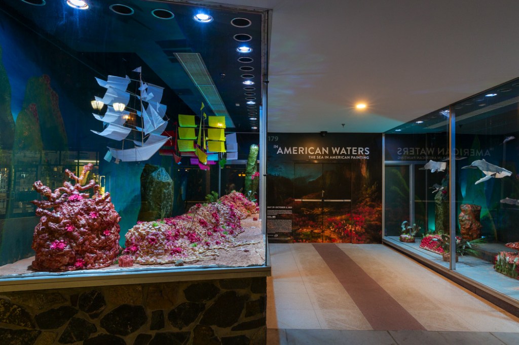 Inside of an exhibition labeled "In American Waters: The Sea in American Painting" with vitrines visible displaying model ships in the sea