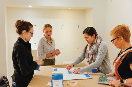 Three students and their professor stand at a table learning how to work on a museum object. 