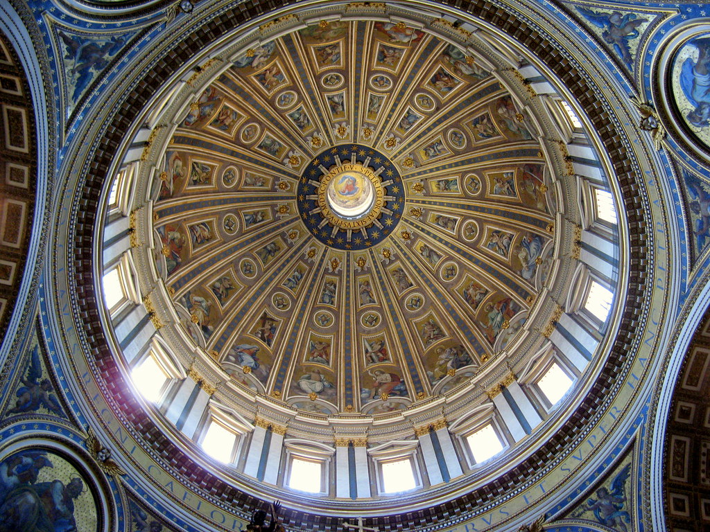 The interior view of a light-filled dome with intricately painted designs arcing up it in columns.