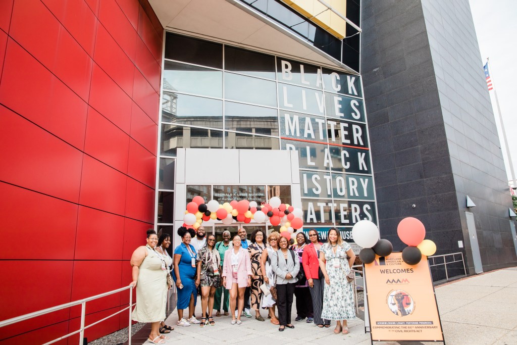 A group photo of people posing in front of a museum building with the text "Black Lives Matter Black History Matters" displayed in the window
