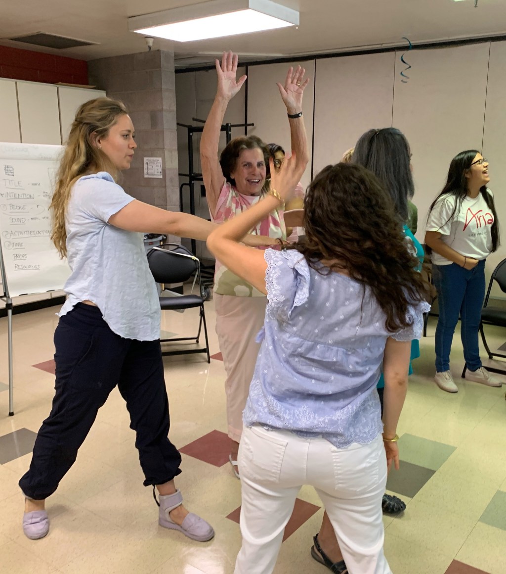 The teaching artist instructs participants who are moving their arms.