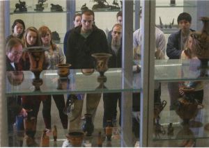A group of people stand looking into a display case. The camera shot is taken through the display case from the other side.