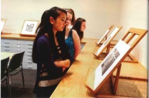 Several young women look at sketches displayed on top of map drawers on small easels. 