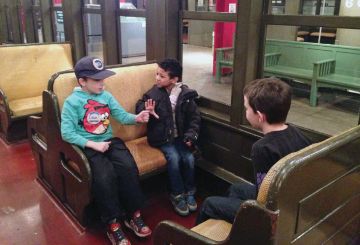 Three boys sit in a train car exhibited in a gallery. 
