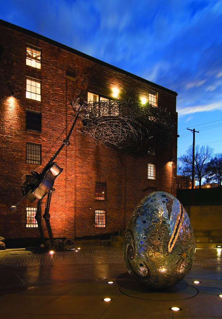 An outdoor plaza with sculptures resembling a bird, nest, and egg made from various materials.