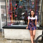 Image of Amanda Figueroa, an white woman sitting in front of a shop window wearing a blue and red dress.