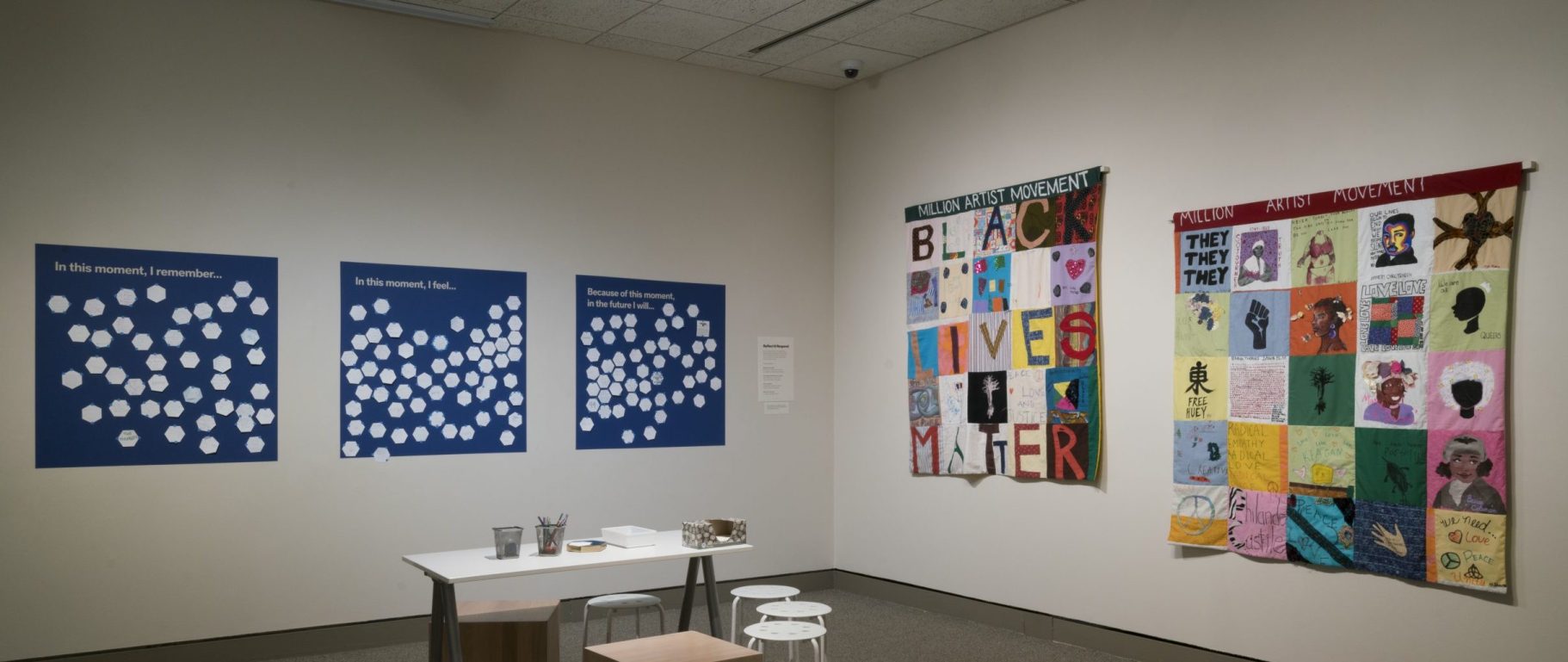 A museum gallery space with Black-Lives-Matter-themed art and a workstation for answering questions on poster boards: "In this moment, I remember...," "In this moment, I feel...," and "Because of this moment, in the future I will..."